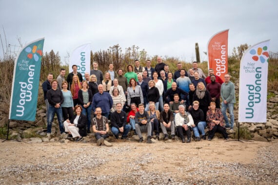 Groepsfoto van medewerkers Waardwonen buiten met banners met nieuwe logo
